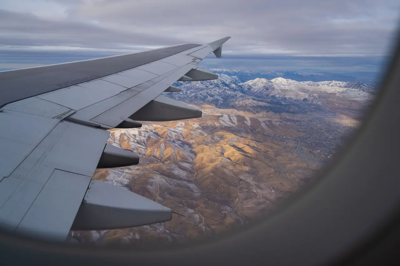 View from a plane window over the wing toward snow-dusted mountain ranges below
