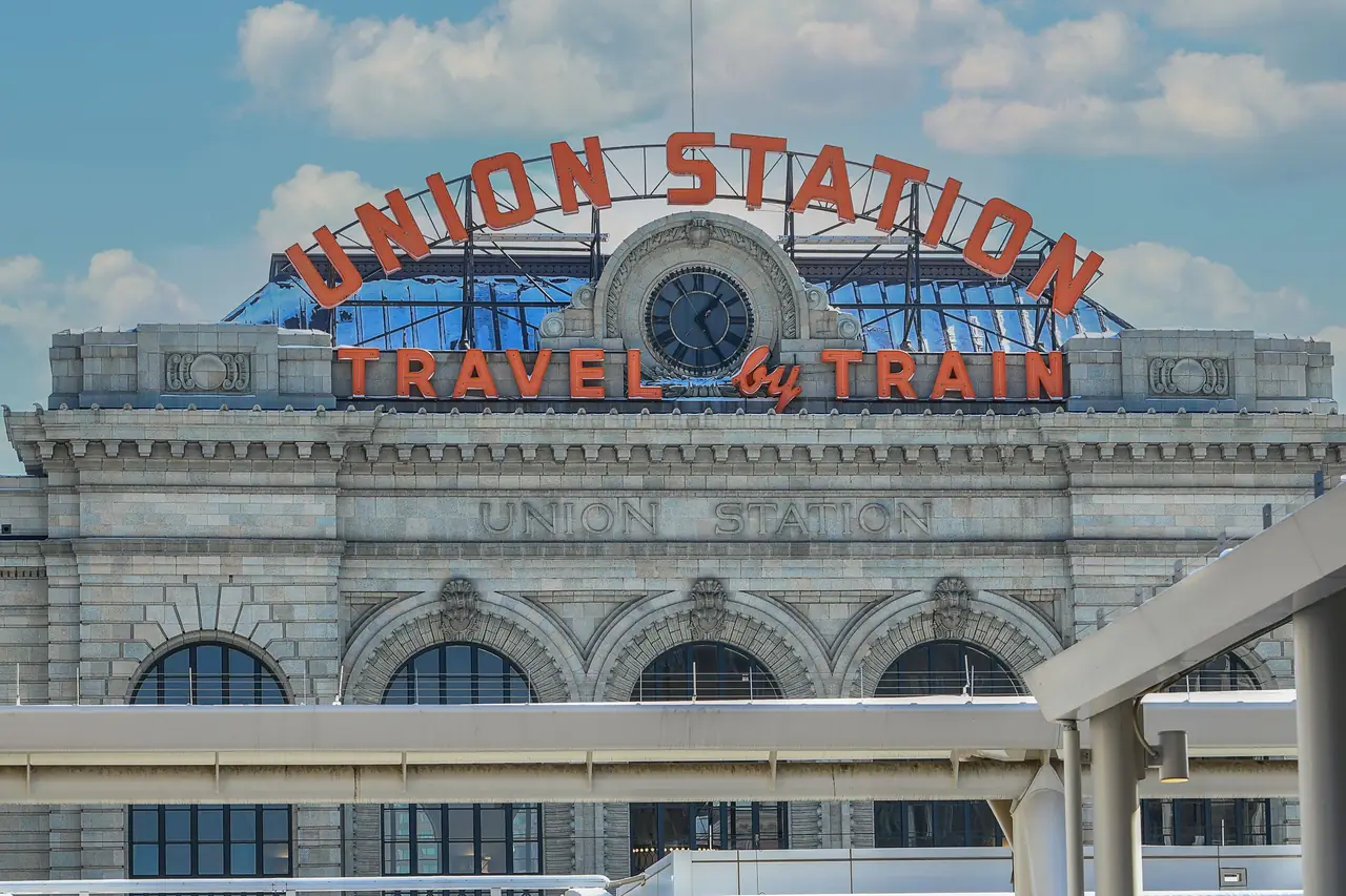 The "Union Station Travel by Train" neon sign and clock above the granite facade of Denver Union Station