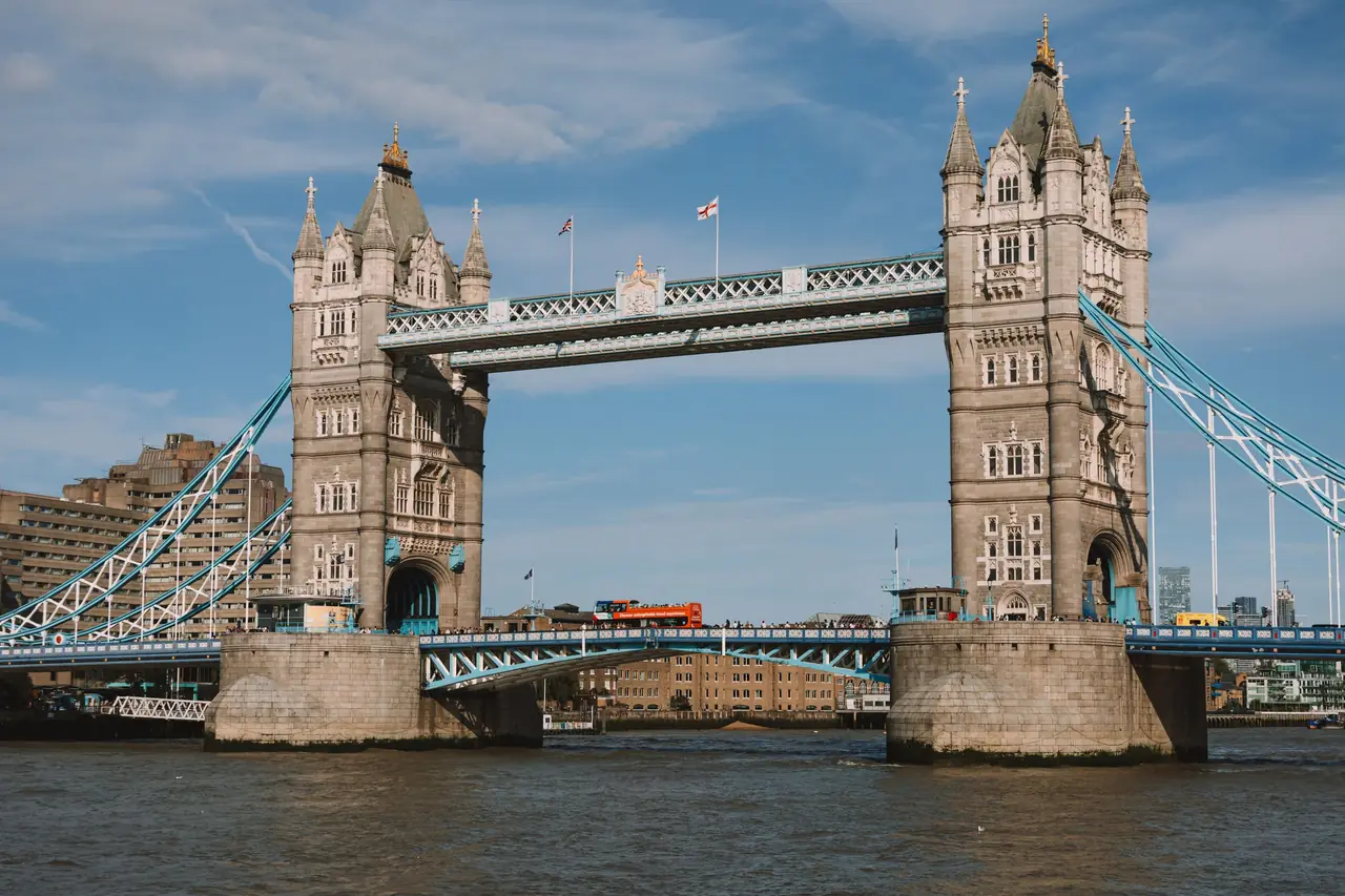 Tower Bridge over the River Thames in London on a sunny day, with a red double-decker bus crossing the span