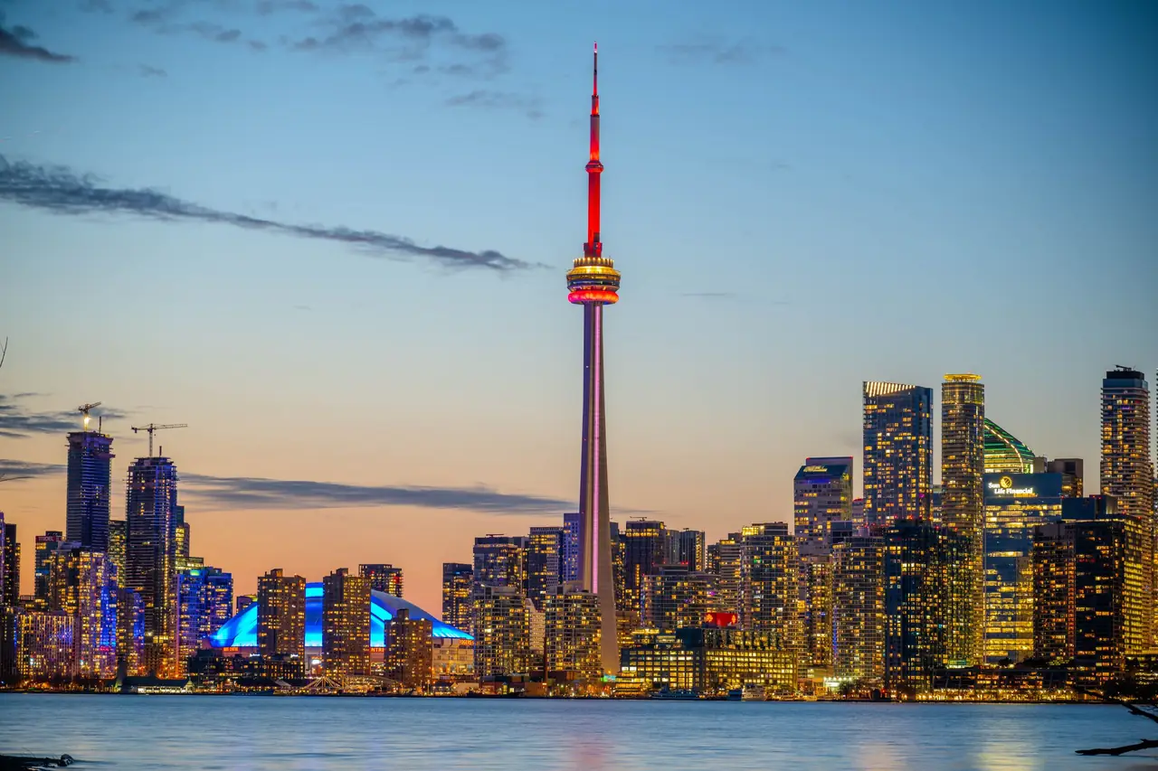 Toronto skyline at dusk across Lake Ontario, with the illuminated CN Tower and Rogers Centre dome