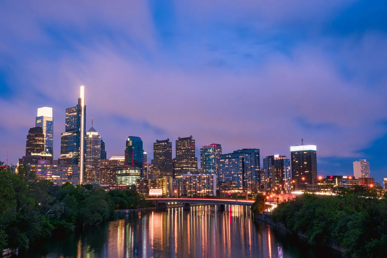 Philadelphia's skyline at dusk over the Schuylkill River, with the Comcast Technology Center's lit spire